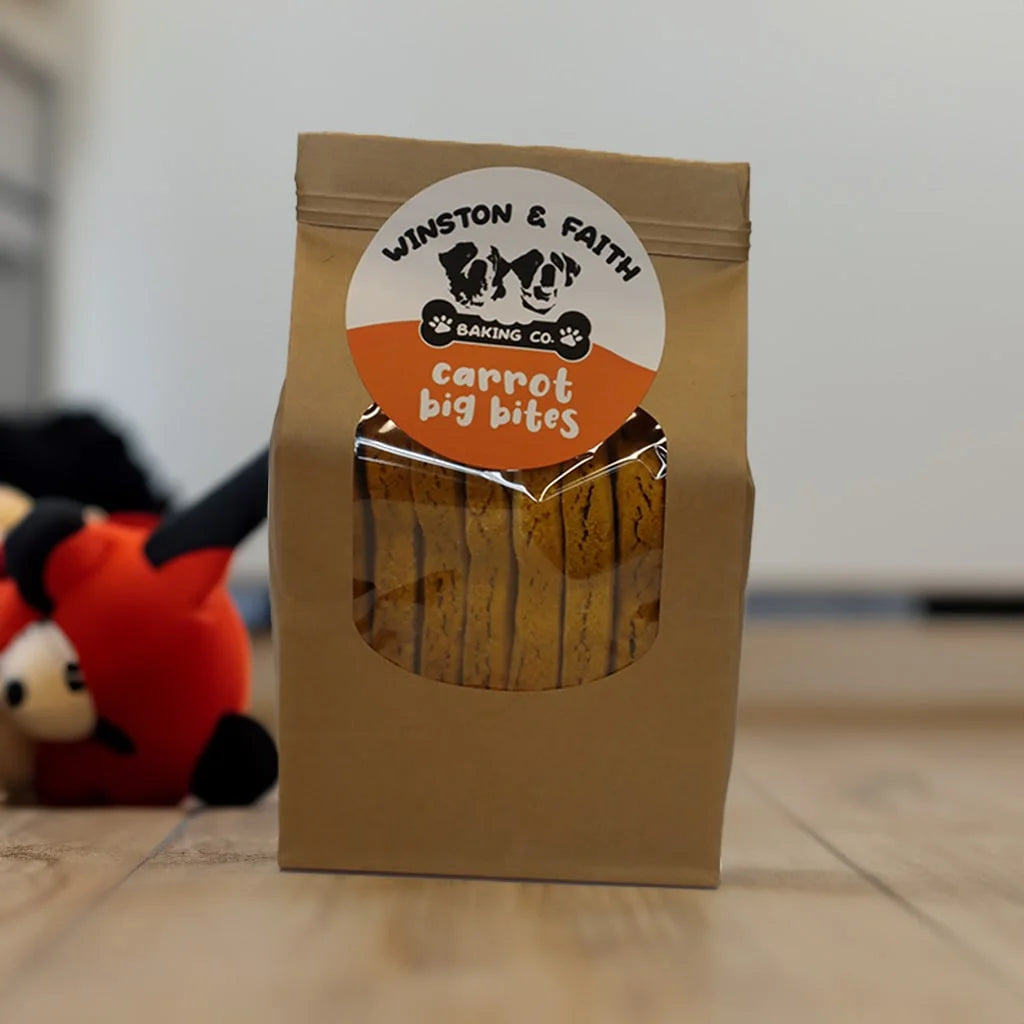 brown packaging bag with a white and orange and white dog treat label on the front. With dog toys in the background.